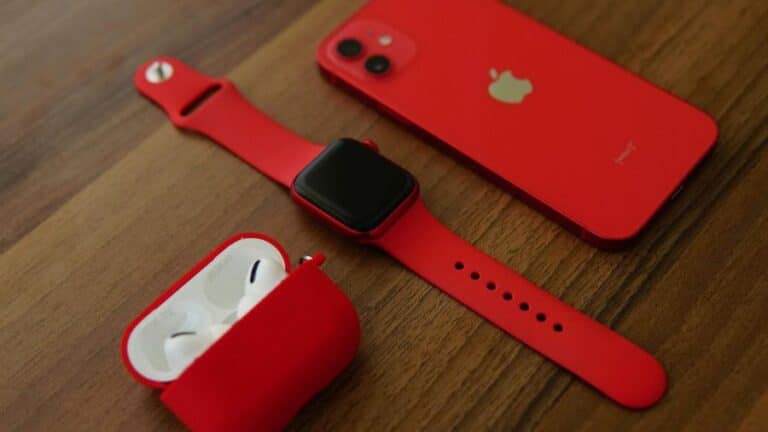 Smartwatch vermelho junto a um iPhone e fones de ouvido, destacando a compatibilidade entre os dispositivos