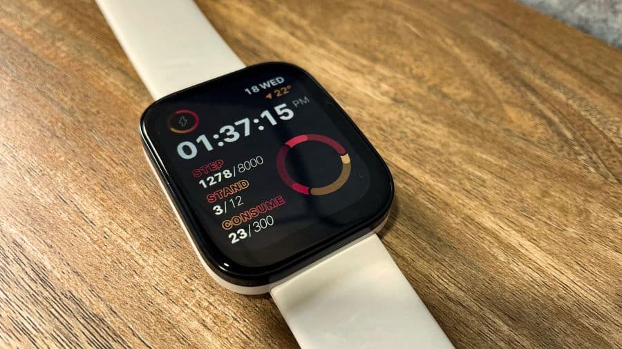 Smartwatch Amazfit Bip 5 com pulseira clara mostrando métricas de saúde na tela, apoiado sobre mesa de madeira