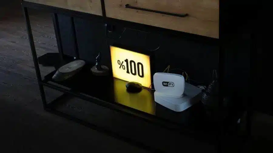Roteador Wi-Fi branco sobre um móvel escuro ao lado de uma placa iluminada