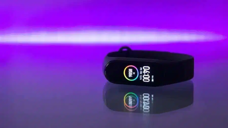 Smartband preta com tela colorida refletindo sobre uma superfície brilhante com fundo roxo iluminado