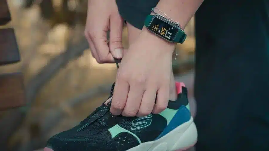 Pessoa usando smartband no pulso enquanto amarra o tênis esportivo antes de um treino ao ar livre
