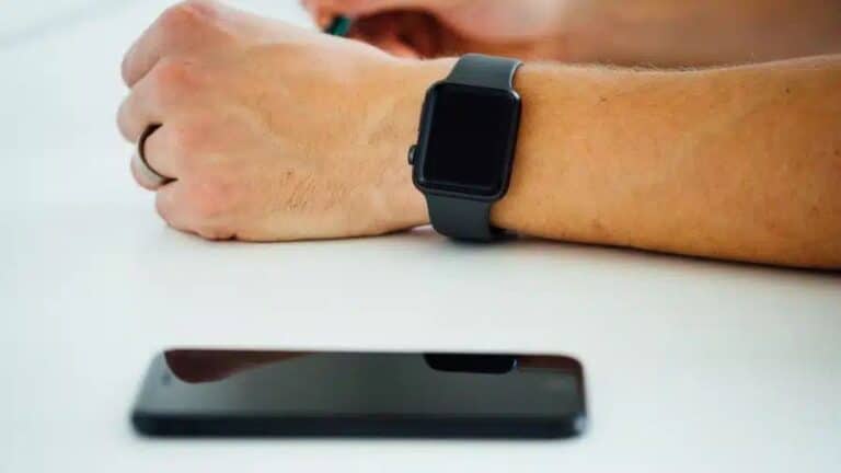 Pessoa com smartwatch no pulso e celular sobre a mesa, simbolizando o uso do relógio sem conexão direta com o telefone