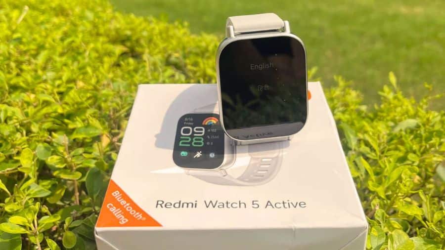 Tela do smartwatch Redmi Watch 5 Active exibindo QR Code para download do aplicativo, com fundo desfocado de grama