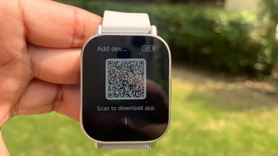 Smartwatch Redmi Watch 5 Active com pulseira clara apoiado sobre sua caixa, em ambiente externo com vegetação ao fundo