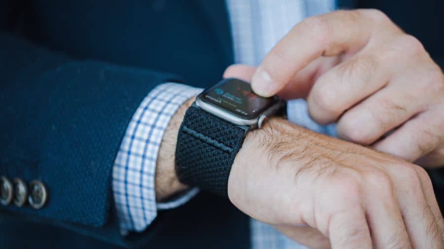 Close-up de smartwatch prateado com pulseira preta sendo usado por homem de terno escuro