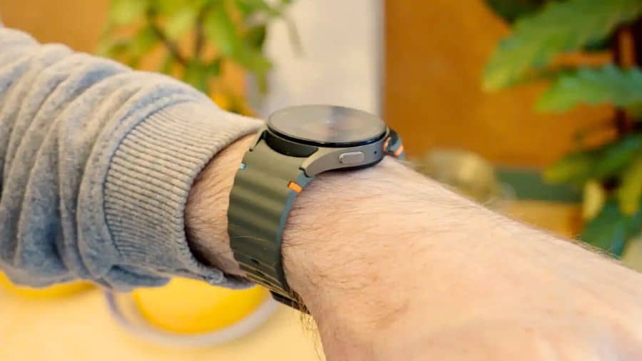 Galaxy Watch 7 no pulso de uma pessoa em ambiente externo, com luz solar destacando o design lateral do relógio